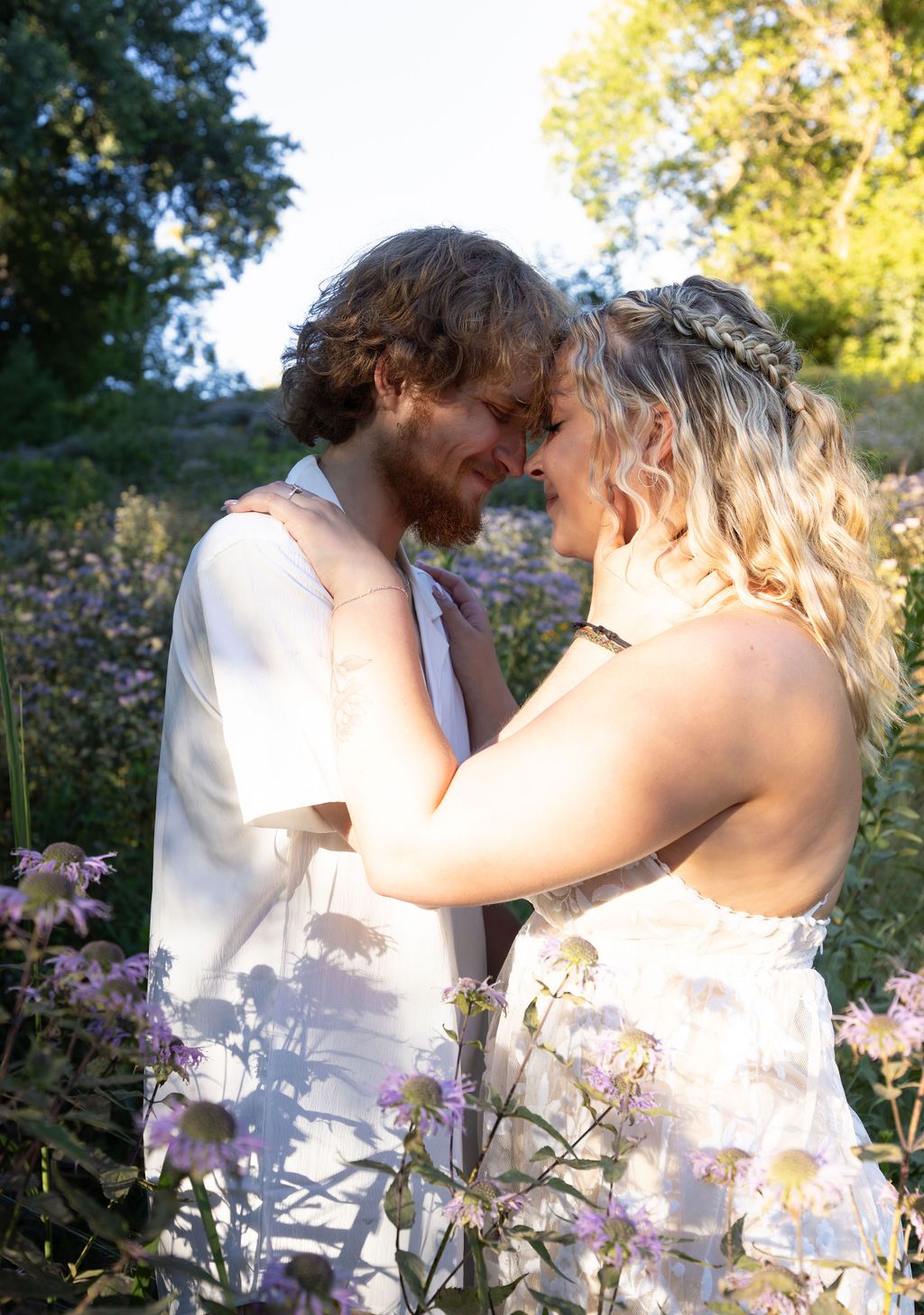 A romantic couple embraces in a wildflower field on a sunny day.