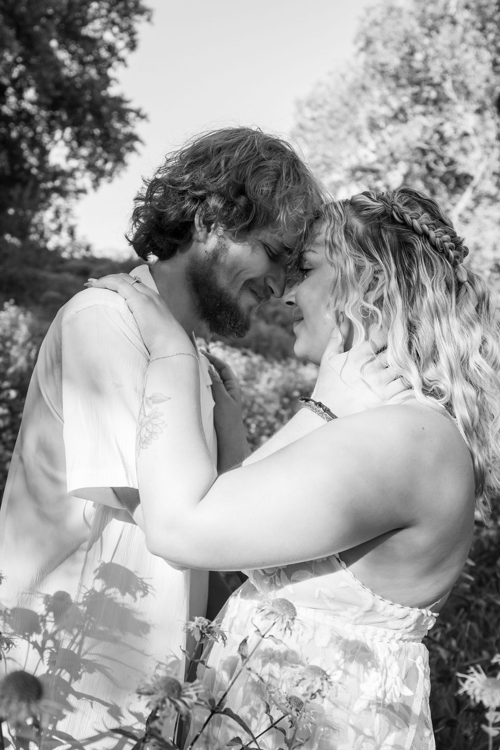 A black and white portrait of a couple sharing an intimate moment outdoors.