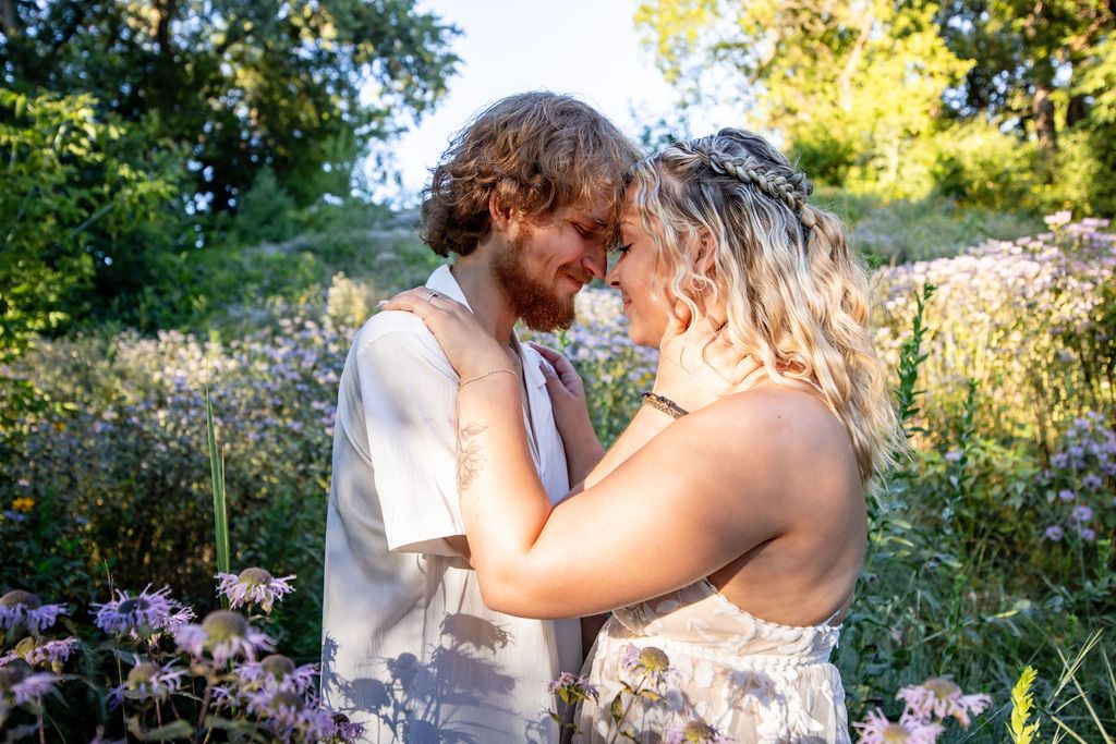 A couple embraces in a sunlit meadow surrounded by purple flowers.