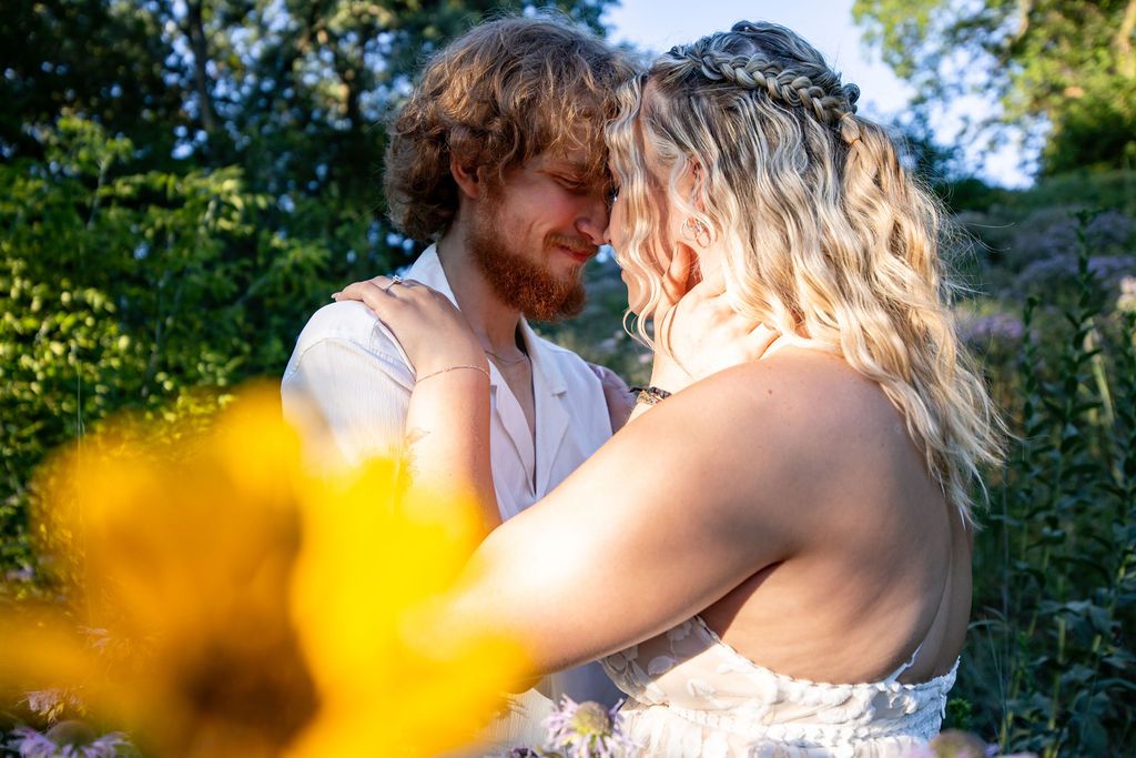 A couple shares a romantic moment in a garden with yellow flowers in the foreground.
