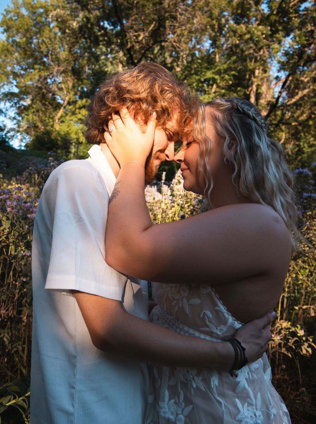 A tender embrace captured in warm sunlight among wildflowers and trees.
