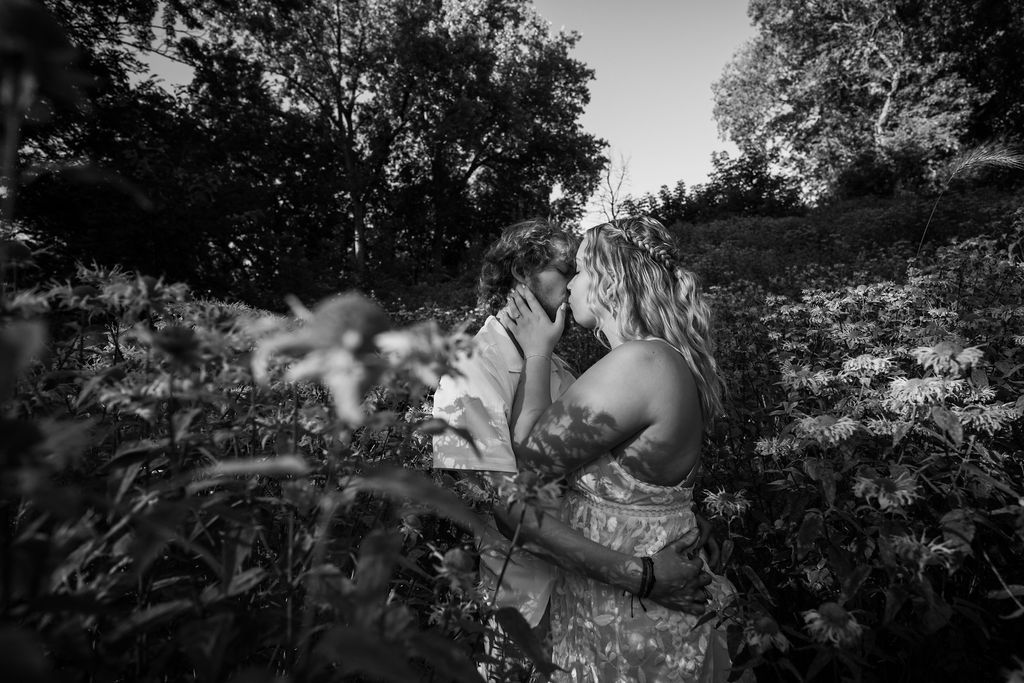 A black and white photo of a couple embracing in a flowering meadow.