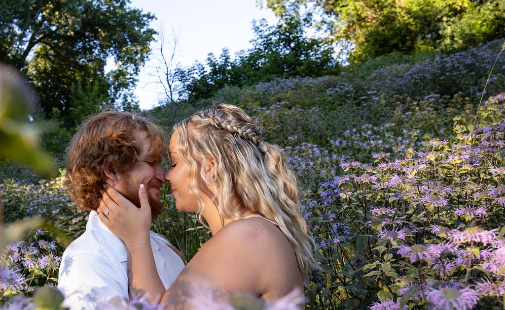 A romantic couple sharing a tender moment among purple wildflowers in a sunlit garden.