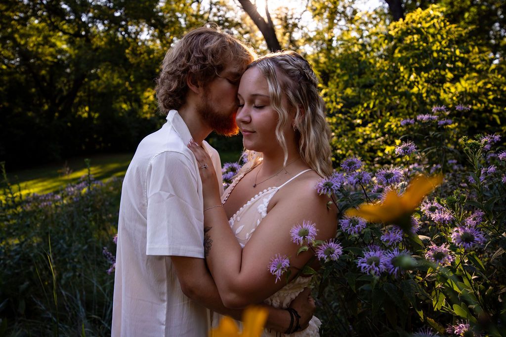 A tender moment between two people in a garden filled with purple flowers at sunset.