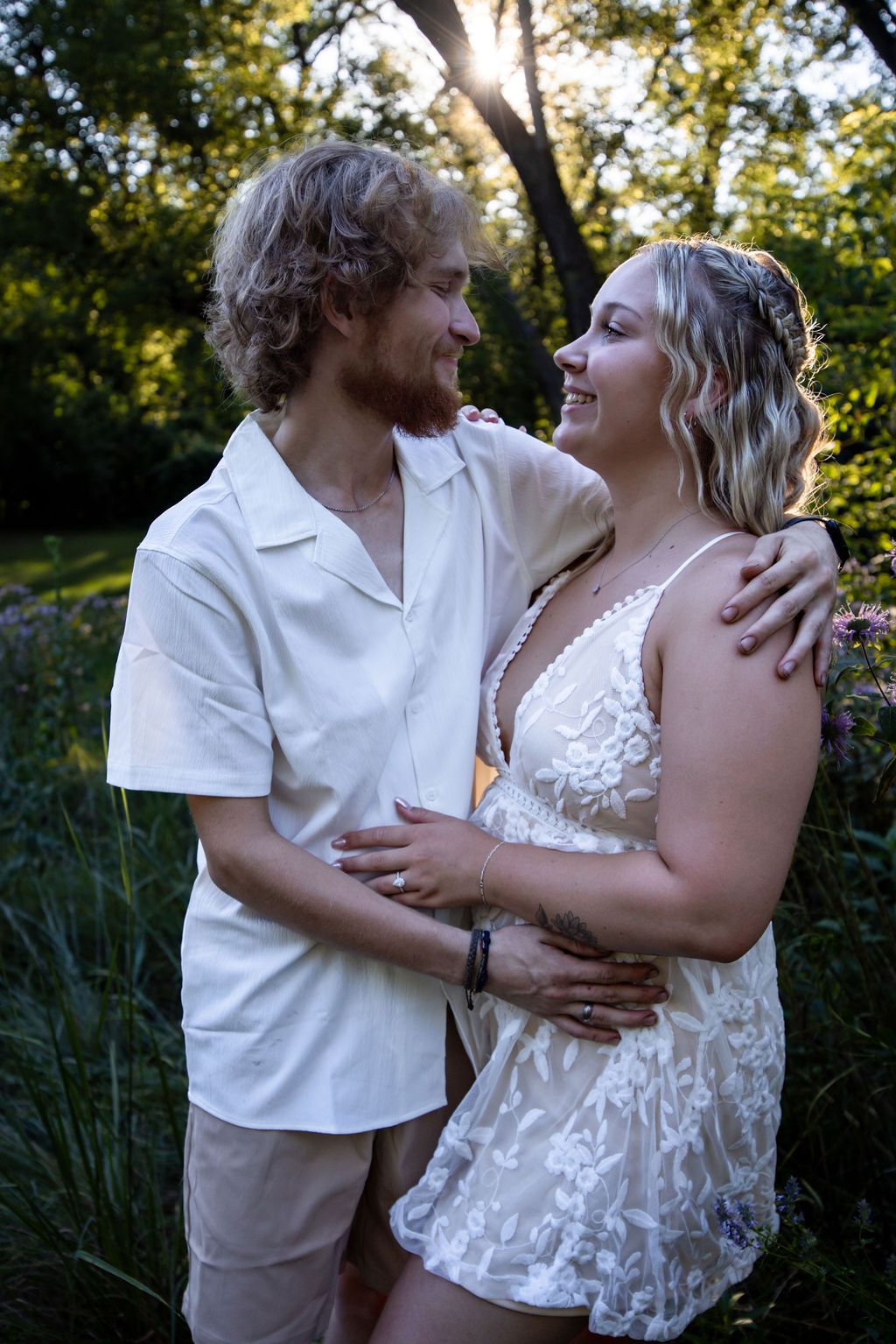Intimate moment between couple in white clothing against lush garden background.