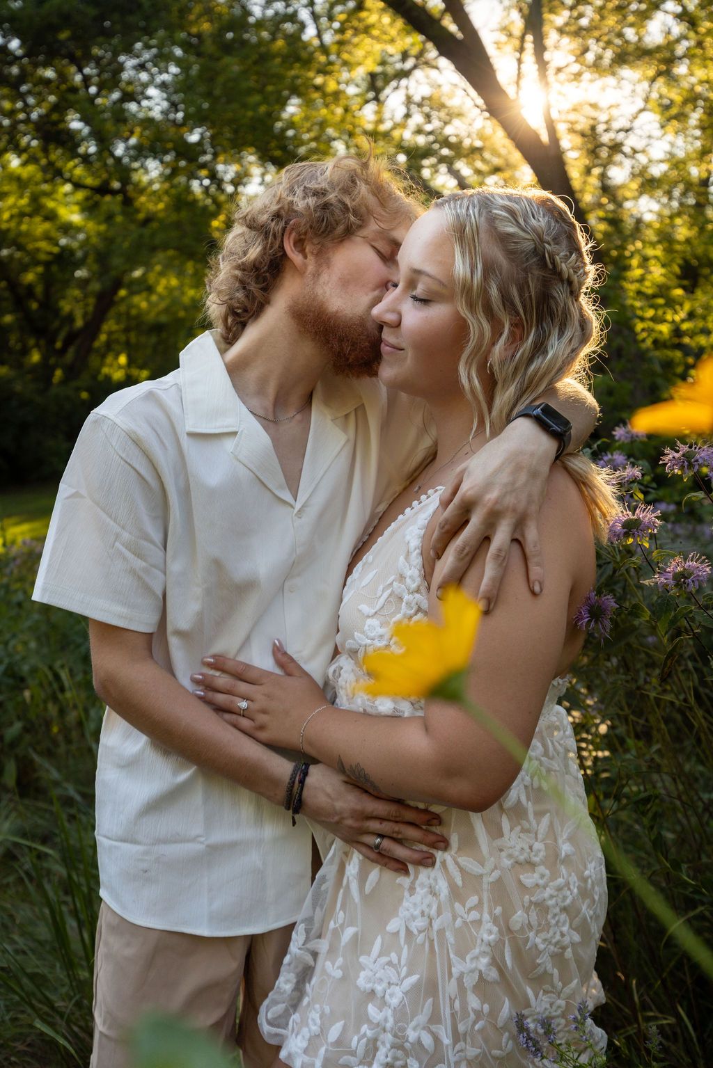 Tender outdoor photoshoot with couple in white outfits among summer foliage.