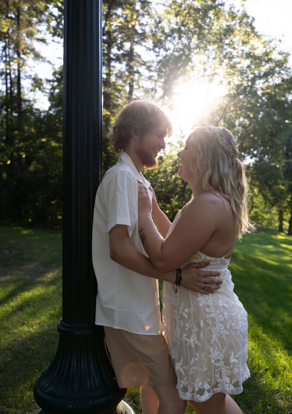Couple shares romantic moment near vintage lamppost in sunny park setting.