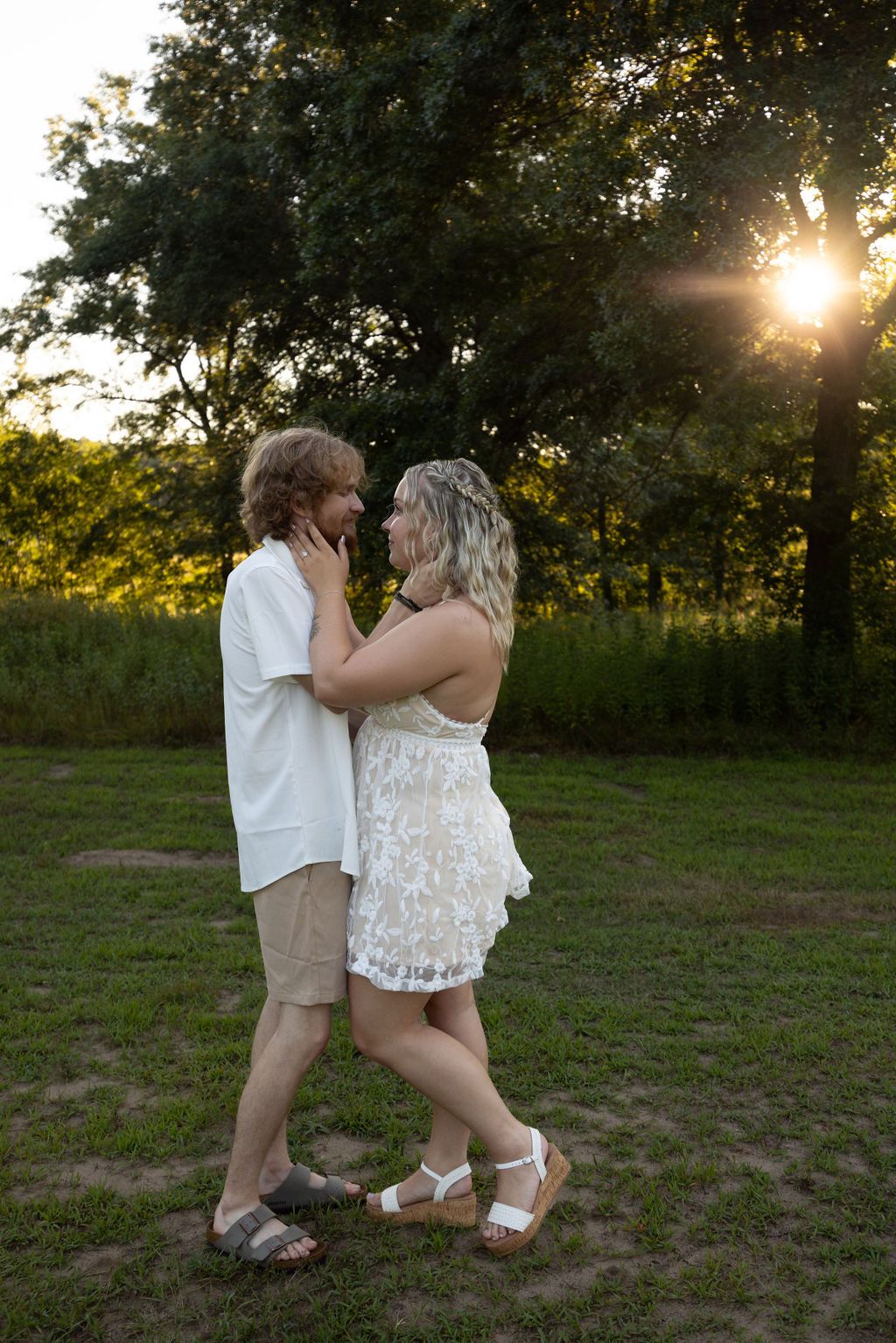 A romantic couple shares an intimate moment at sunset in an outdoor field setting.