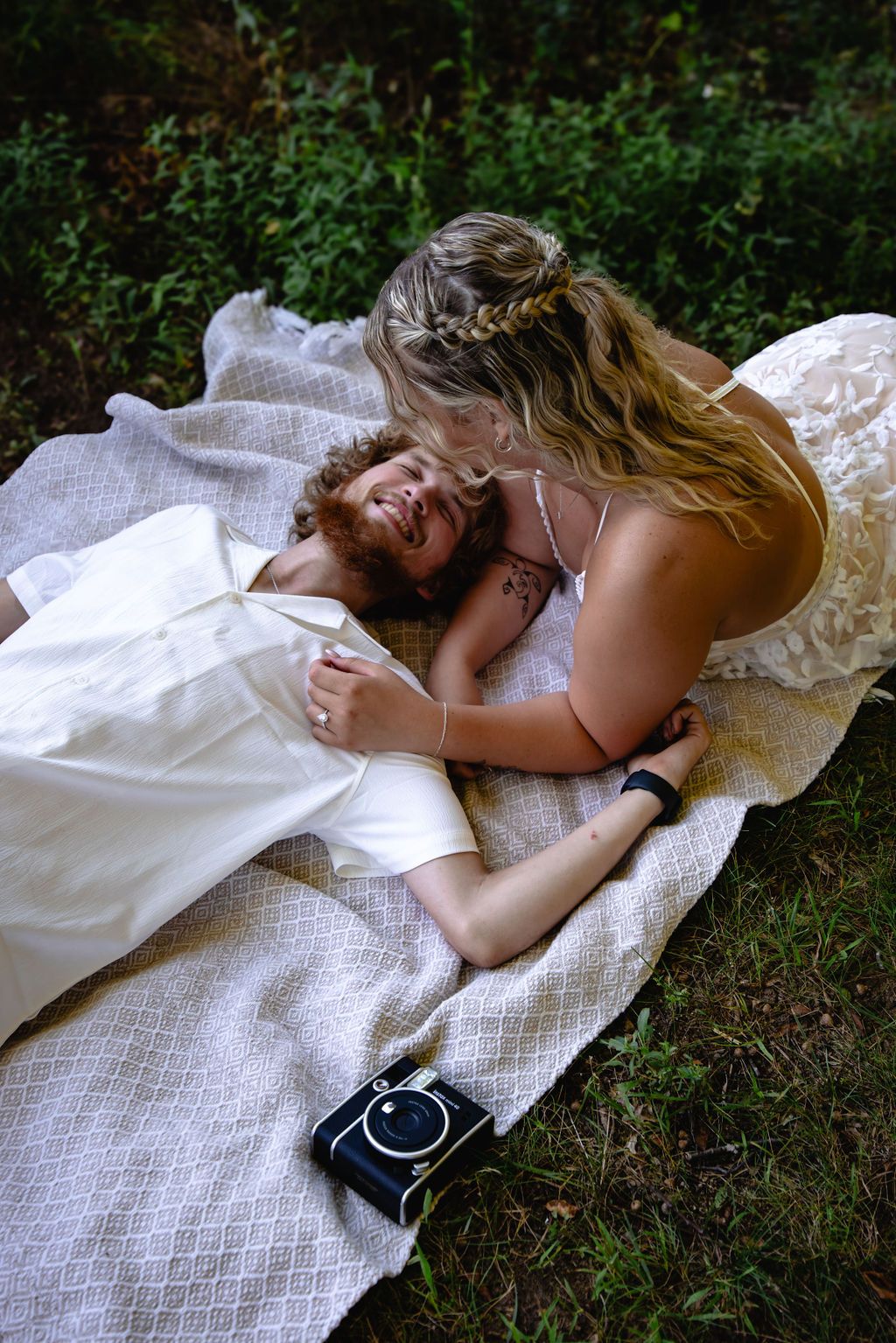 Couple lying together on a white blanket in a garden setting.