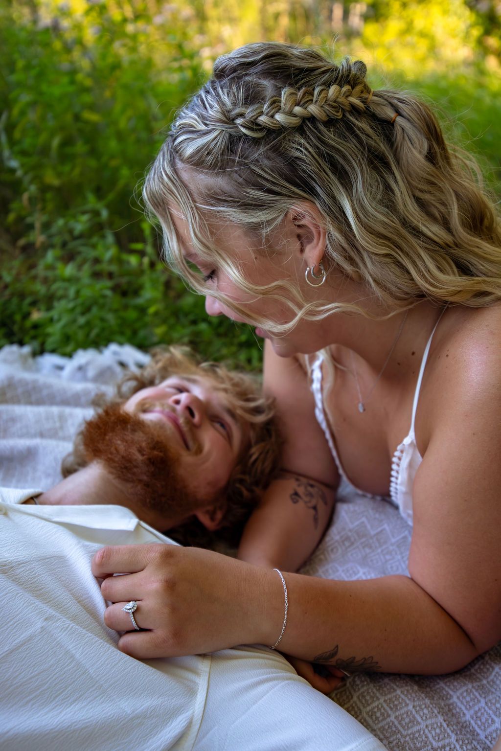 Intimate portrait of a couple sharing a tender moment on a white blanket outdoors.
