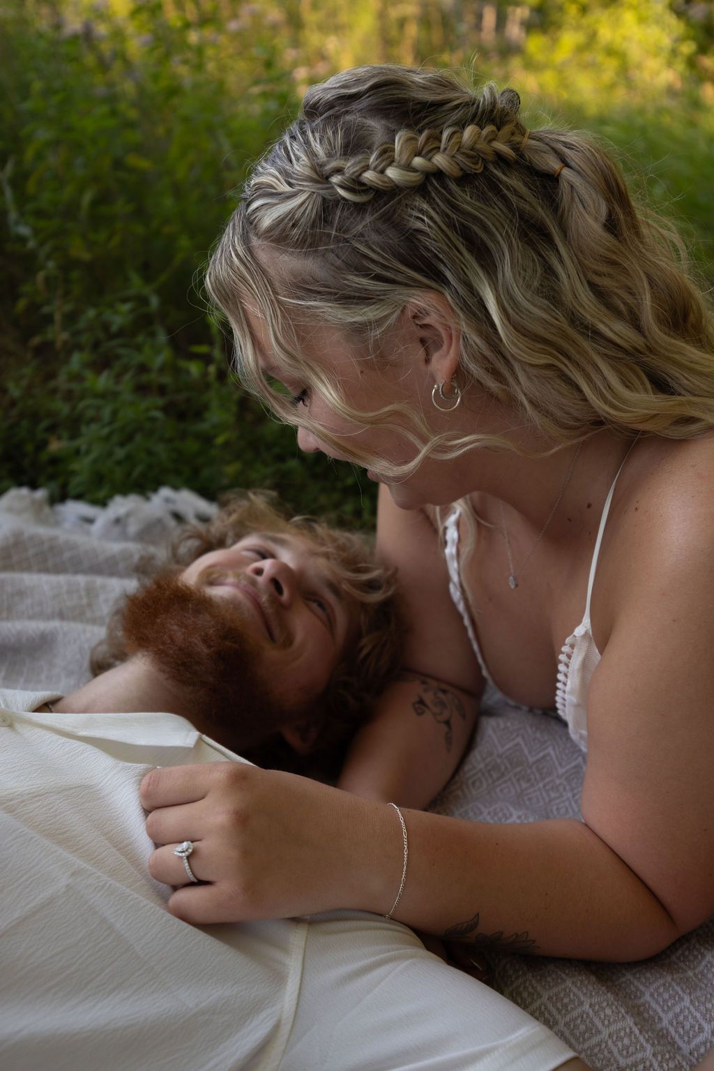 A romantic couple sharing an intimate moment on a blanket outdoors with golden sunlight in the background.