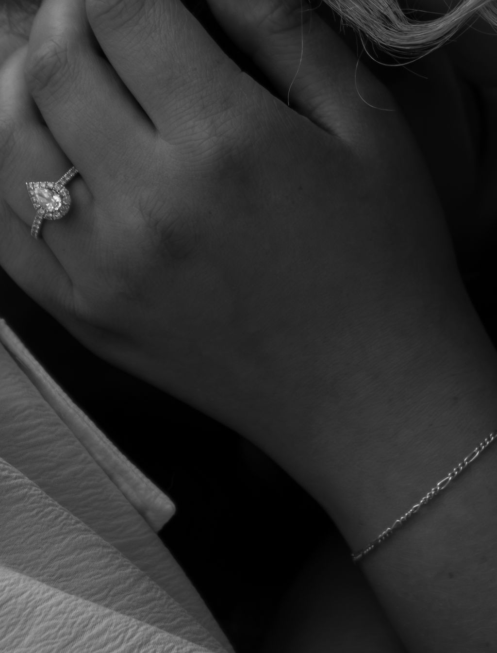Close up of an elegant diamond engagement ring and bracelet on a hand against white fabric.