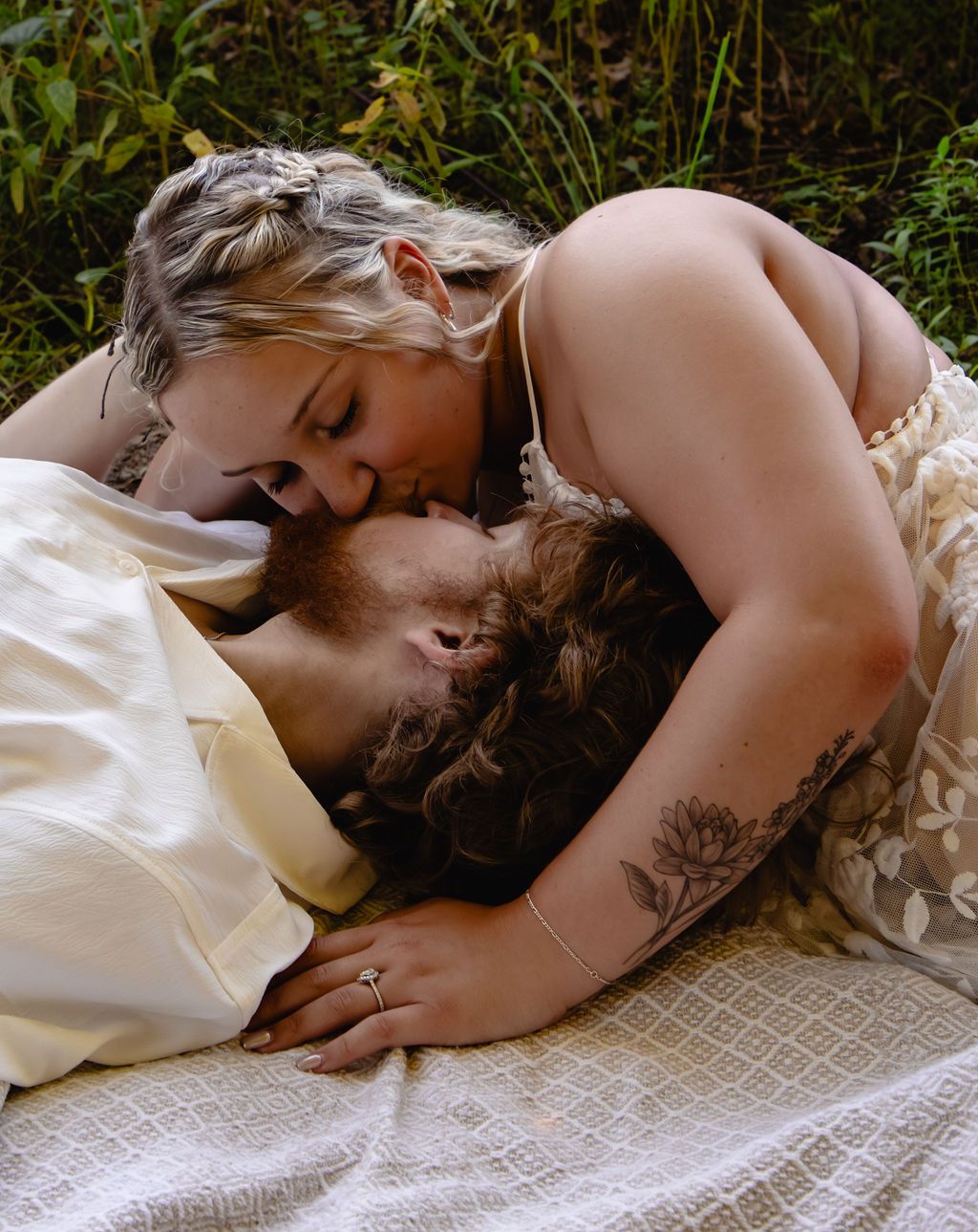 An intimate portrait of a couple embracing while resting on a white blanket outdoors.