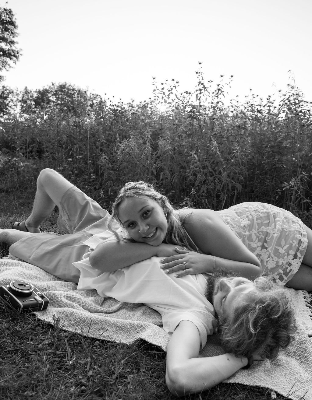 Black and white photo of a couple relaxing together on a blanket near wild grasses.