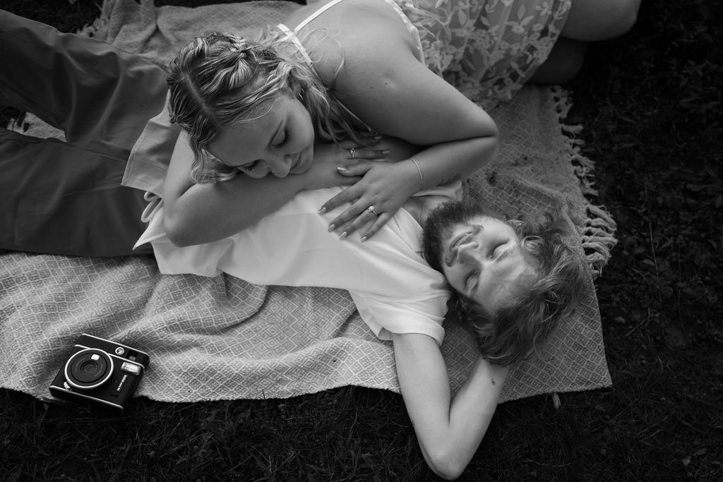 An artistic black and white photo of a couple resting on a blanket with a camera nearby.