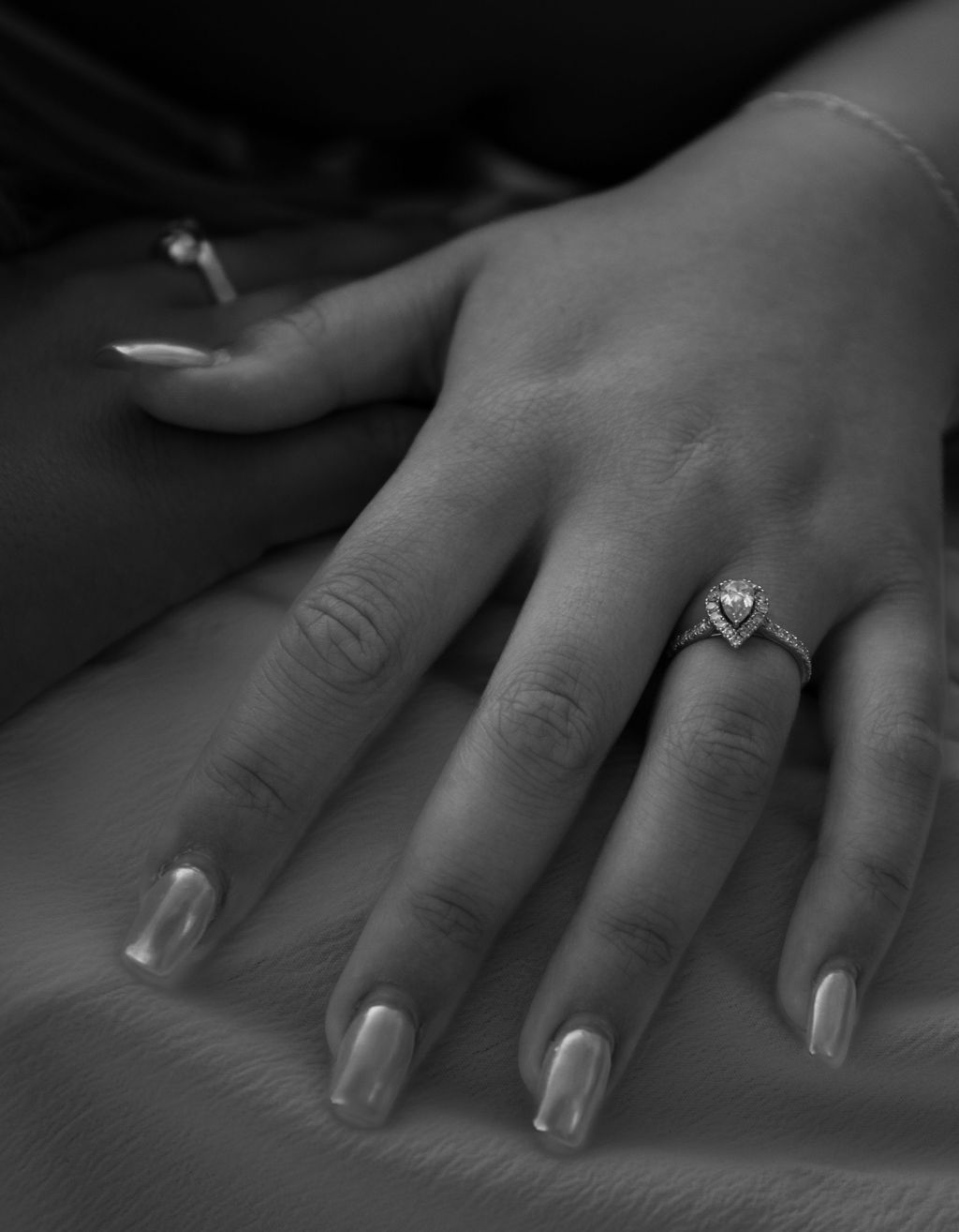 Close-up of a hand with manicured nails wearing an elegant diamond engagement ring.
