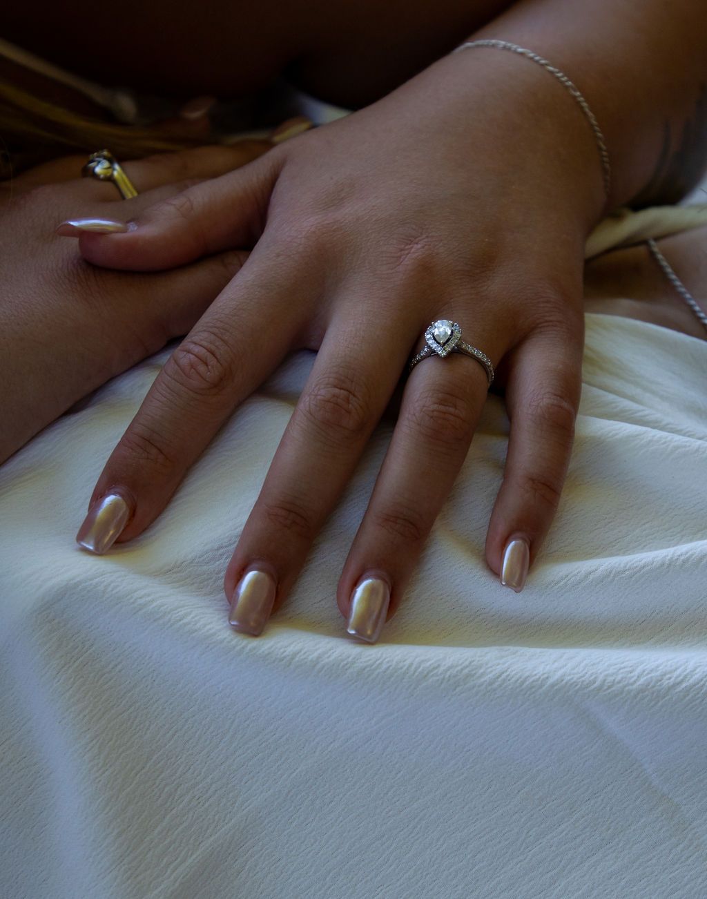 Elegant hand with neutral nail polish and engagement ring against white textured background.
