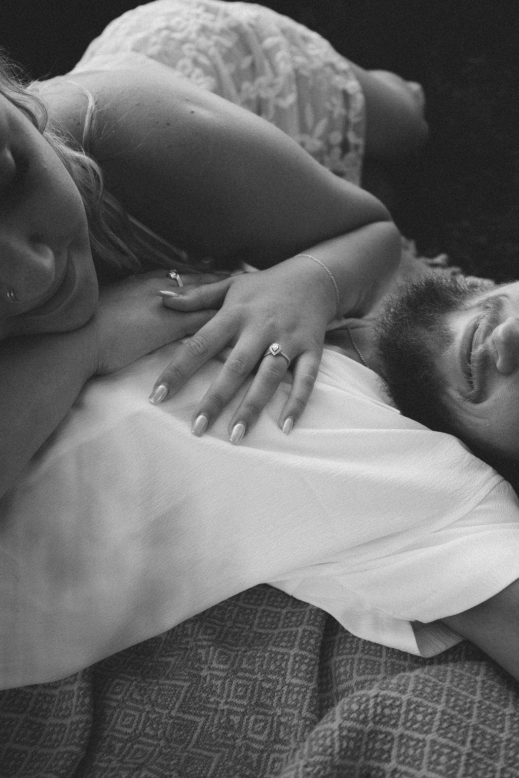 Intimate black and white photograph showing hands with engagement ring on white clothing.