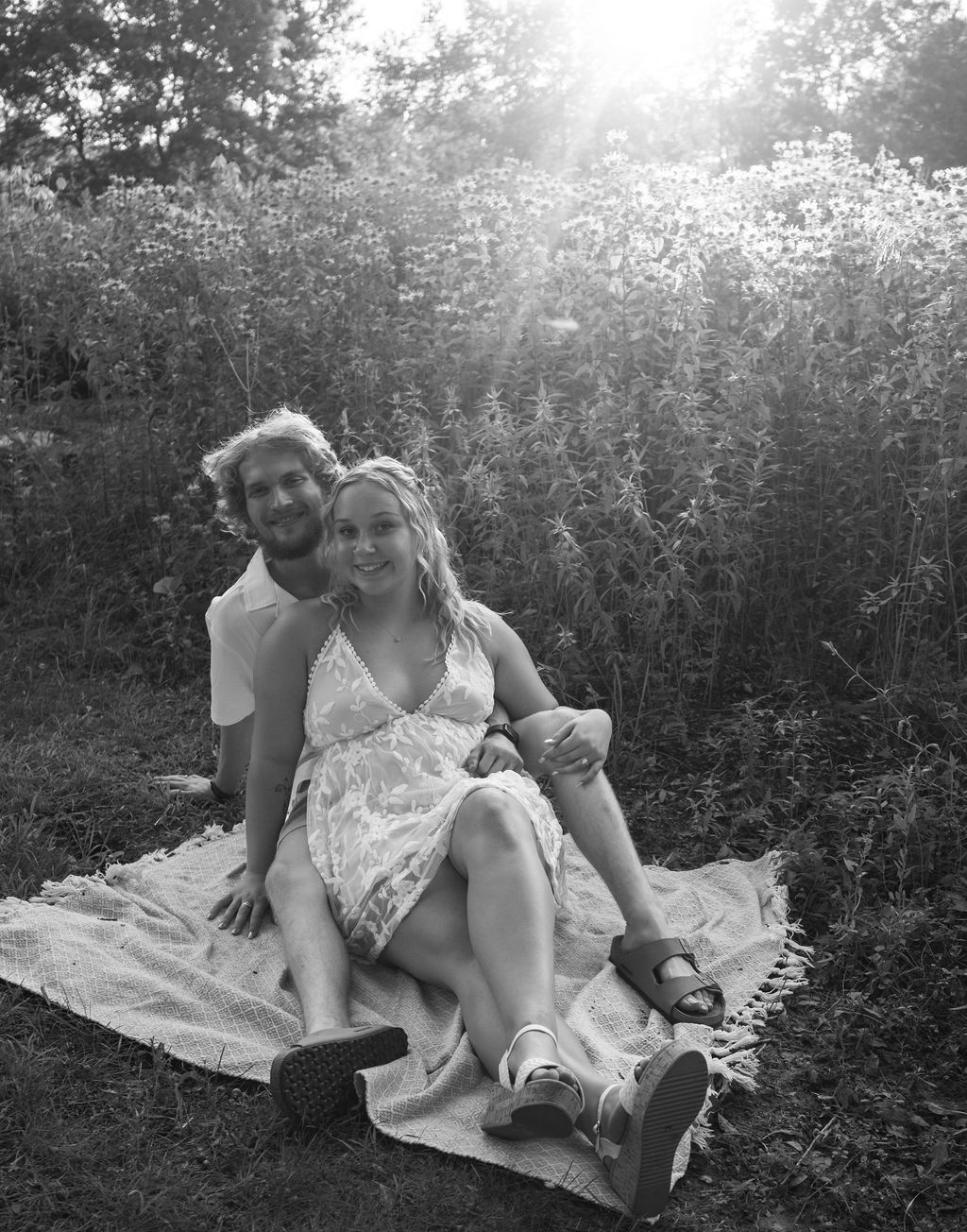 Couple sitting on blanket in wildflower field during golden hour.