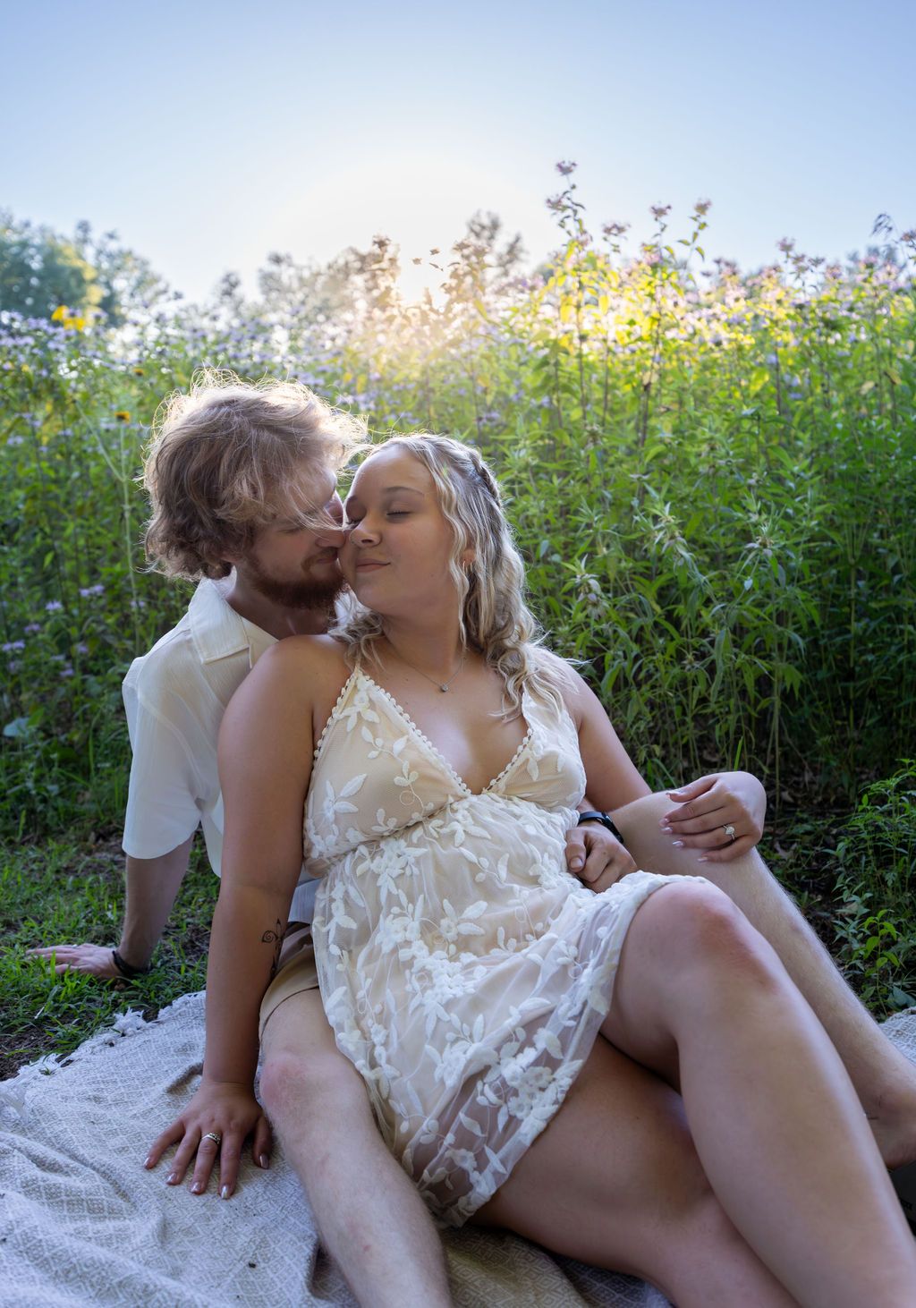 Sunlit outdoor portrait of couple embracing among blooming wildflowers.