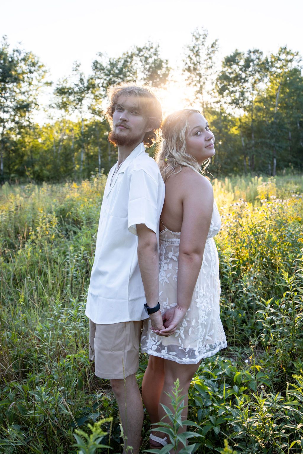 Couple shares tender moment among tall grass and wildflowers at sunset.