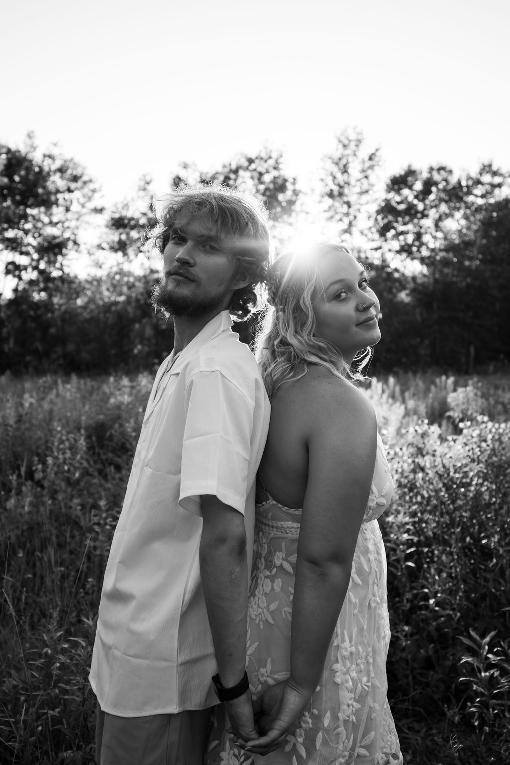 Black and white portrait of couple standing back to back in a summer field.