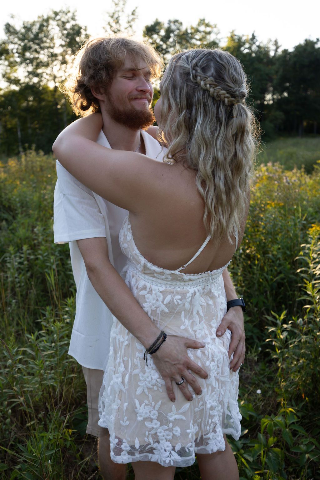 Close up of couple embracing in field with white lace dress detail.