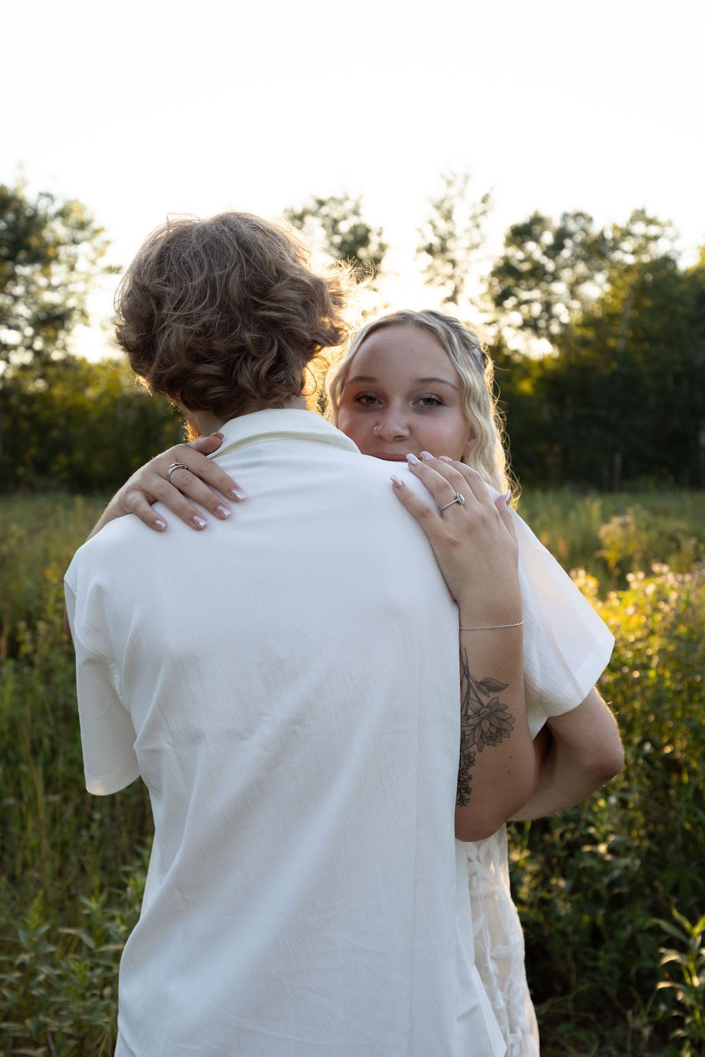 Gentle embrace captured from behind with sunlight filtering through trees.