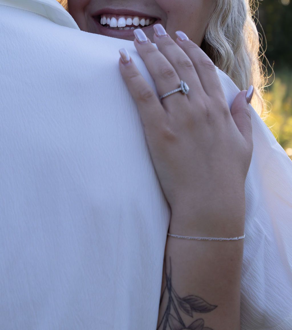 Close up detail of hands with engagement ring and tattoo against white fabric.