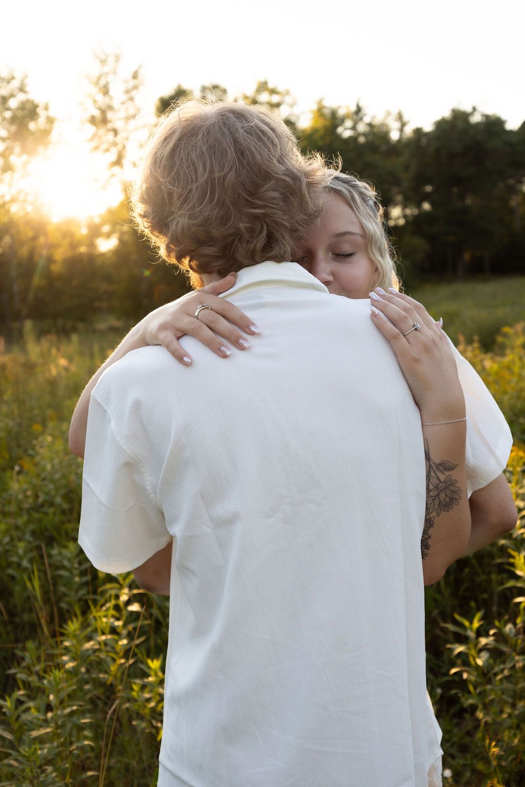 A gentle hug shared between two people in a sunlit meadow with golden wildflowers.