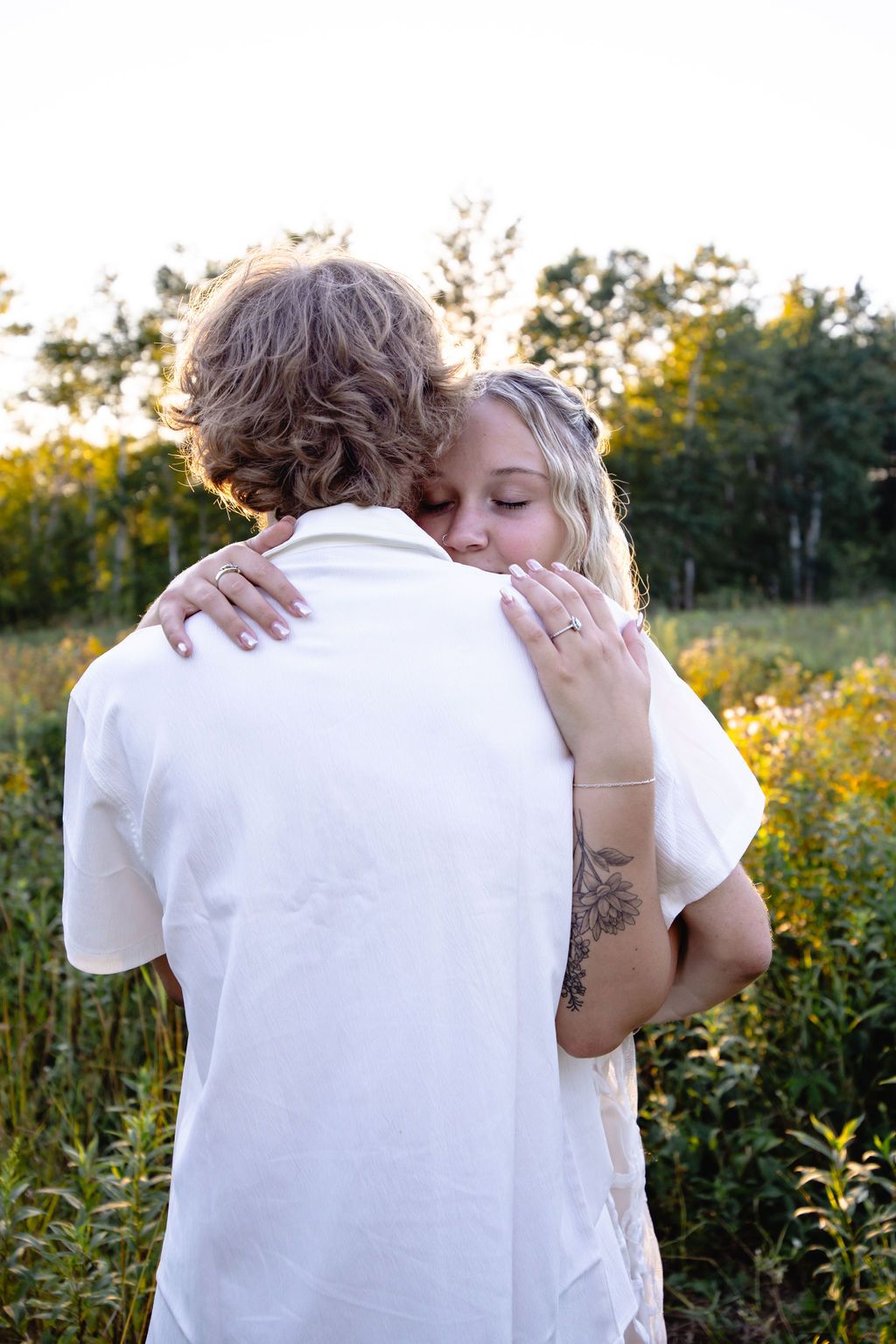 Two people share an intimate embrace in a wildflower field during golden hour.