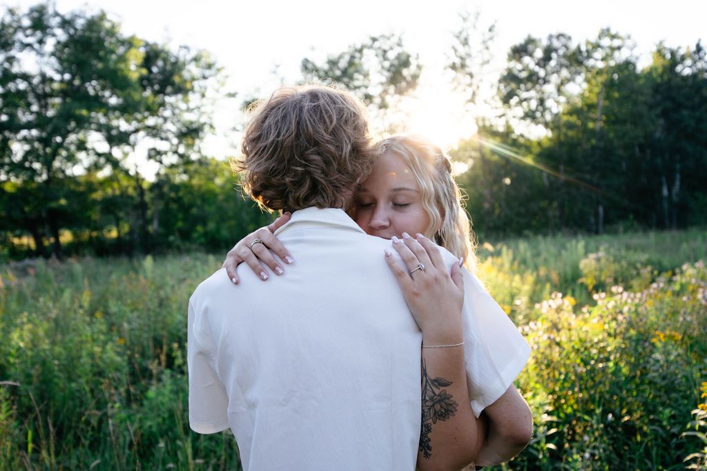 An emotional embrace captured in a sun-drenched field surrounded by summer foliage.