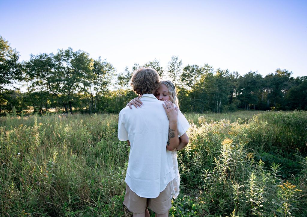 A romantic moment photographed in a serene meadow with blue sky and setting sun.