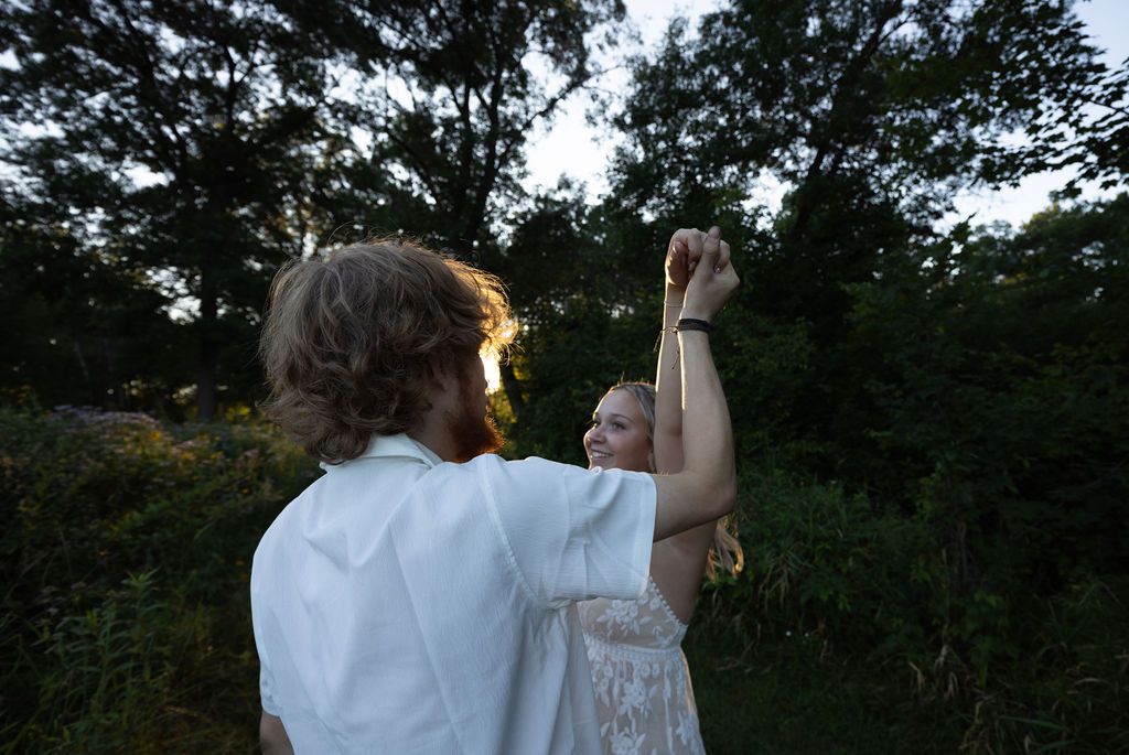 A couple dancing in a field at sunset with light streaming through trees.