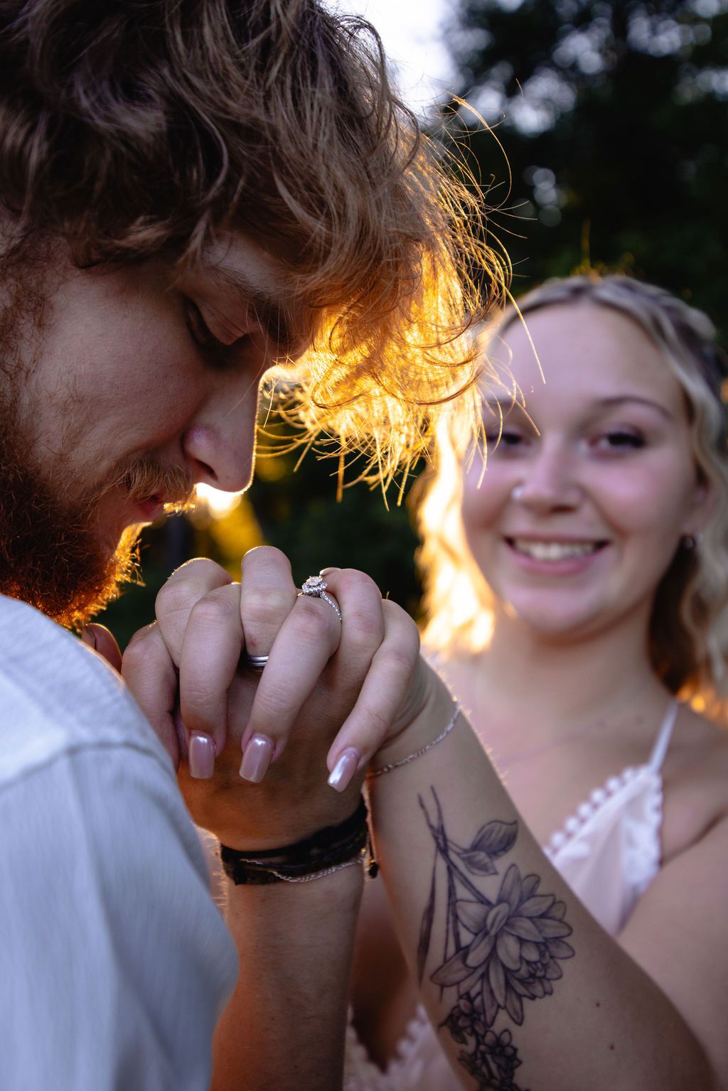 Sunlit romantic moment in nature with rings and floral tattoo visible.