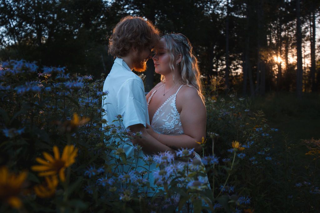 Romantic couple portrait in wildflower field with sunset filtering through trees.