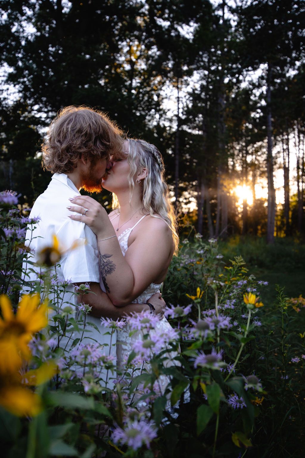 Sunset engagement photo with couple embracing in field of purple and yellow flowers.