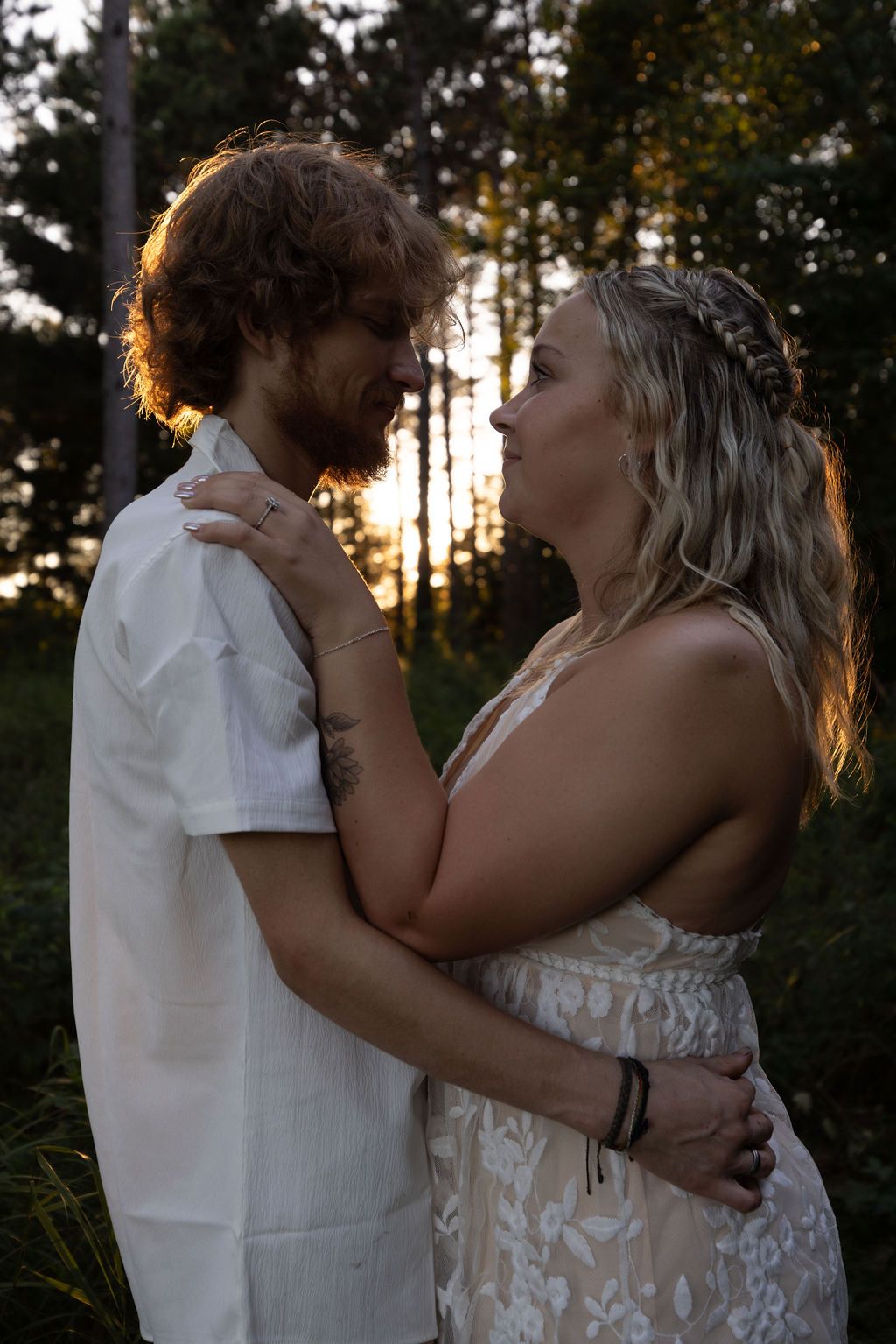 A romantic sunset engagement photo of a couple embracing in a forest setting with dramatic backlighting.