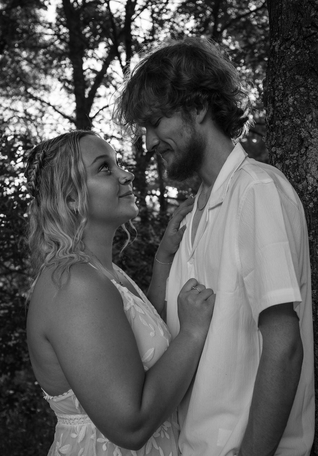 Black and white close-up of a couple in white clothing sharing an intimate moment against forest backdrop.