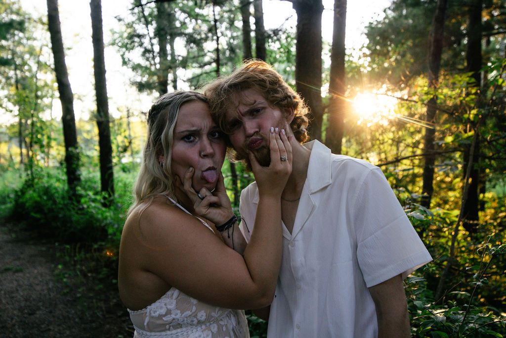 Couple in white outfits making funny faces during their forest photo session at sunset.