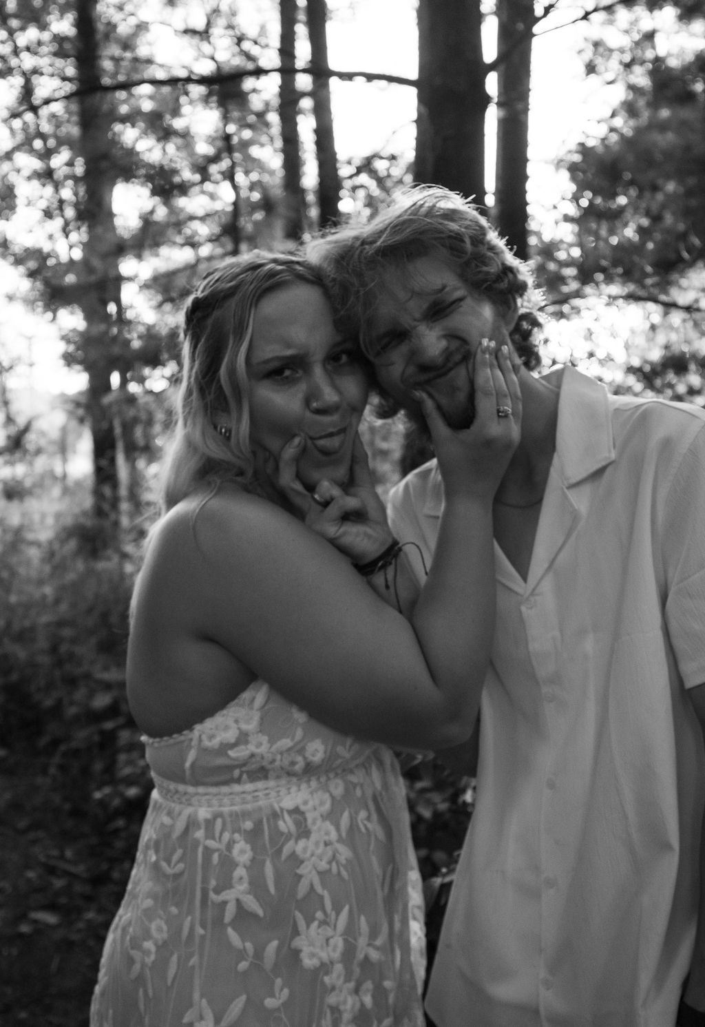 Black and white portrait of a couple playfully posing and laughing in a forest setting.
