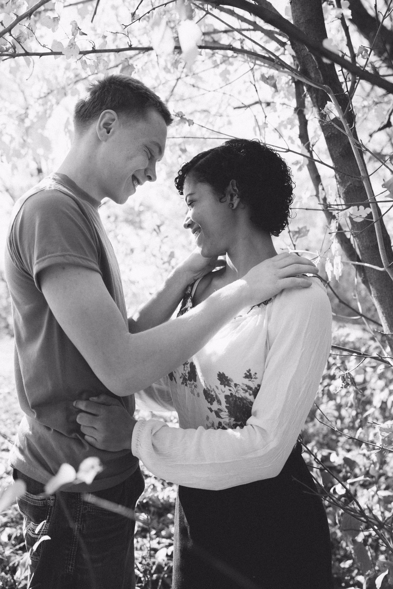 A black and white photo captures an intimate moment between a couple among blooming trees.