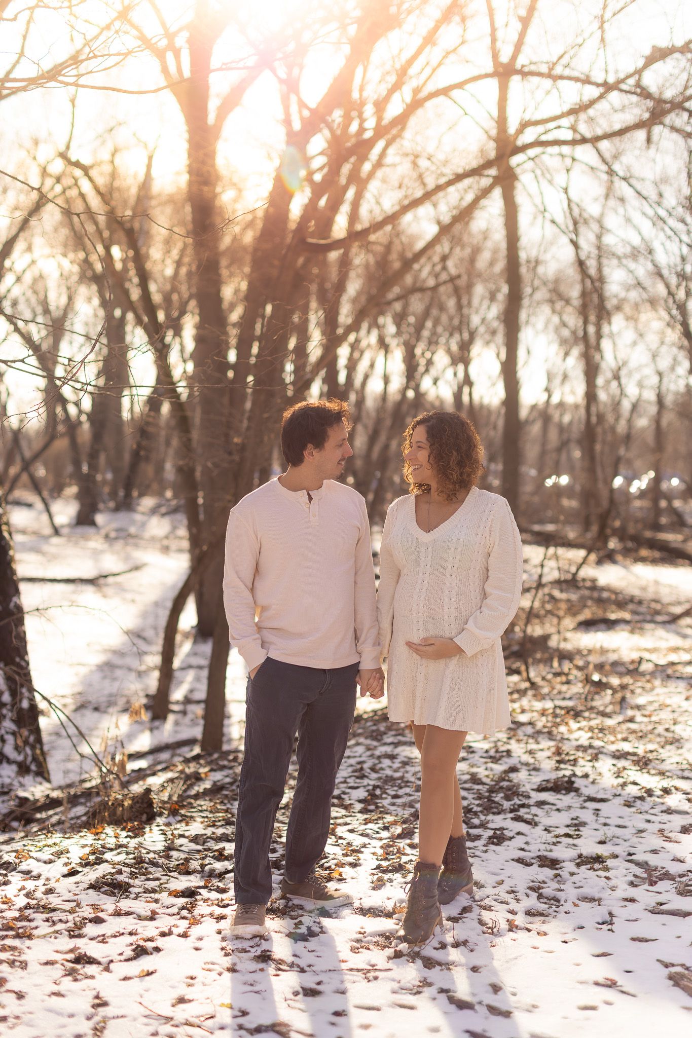 A couple walks hand in hand through a snowy forest path at sunset creating a romantic winter scene.