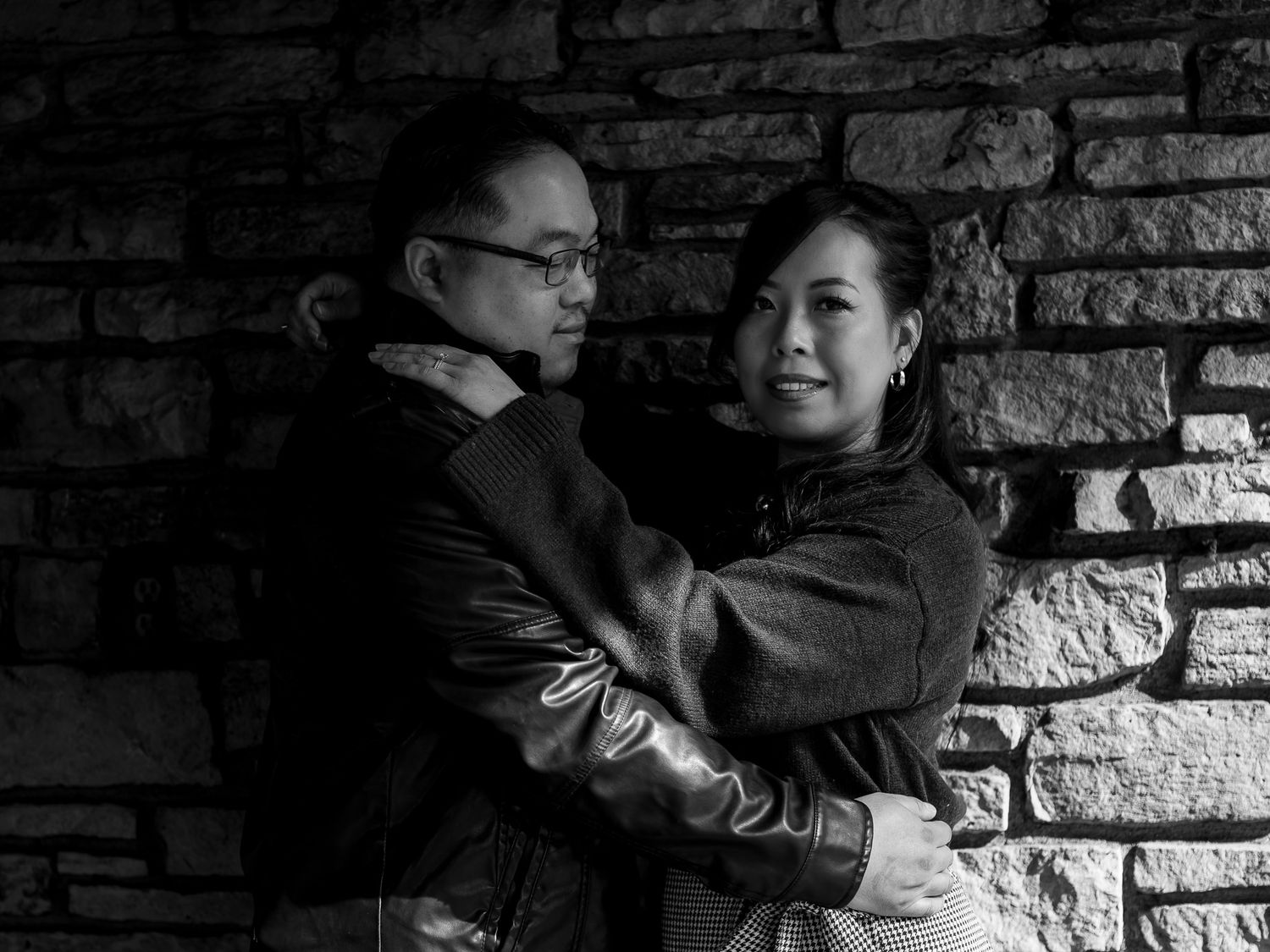 A romantic black and white engagement photo series showing a couple embracing against a stone wall background.