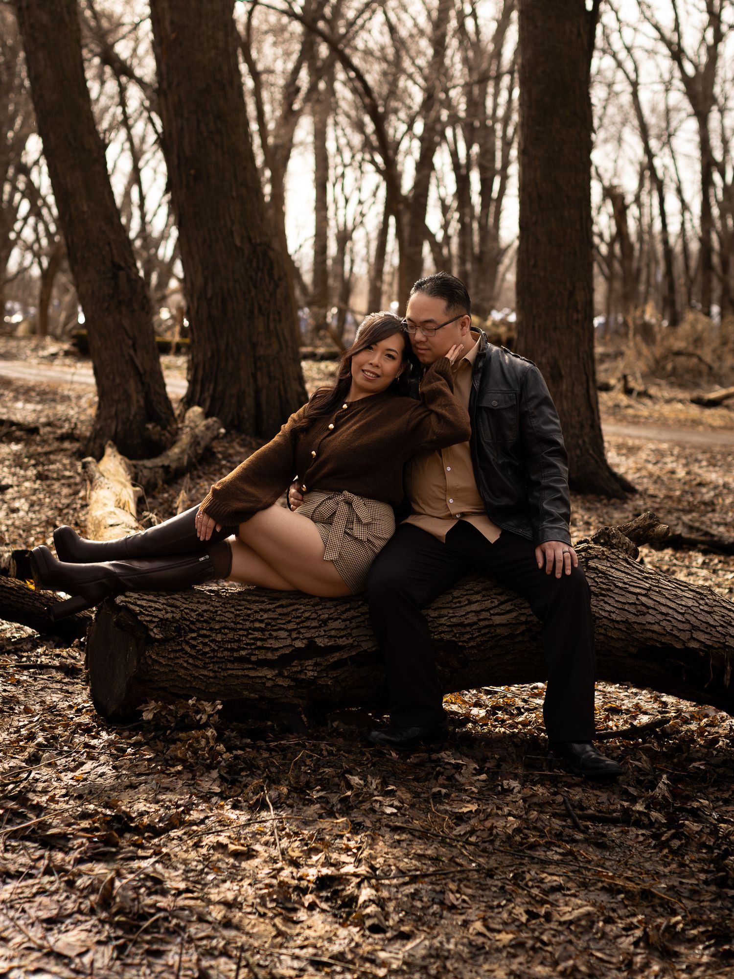 A couple shares an intimate moment lying together on a fallen tree trunk in an autumn forest setting.
