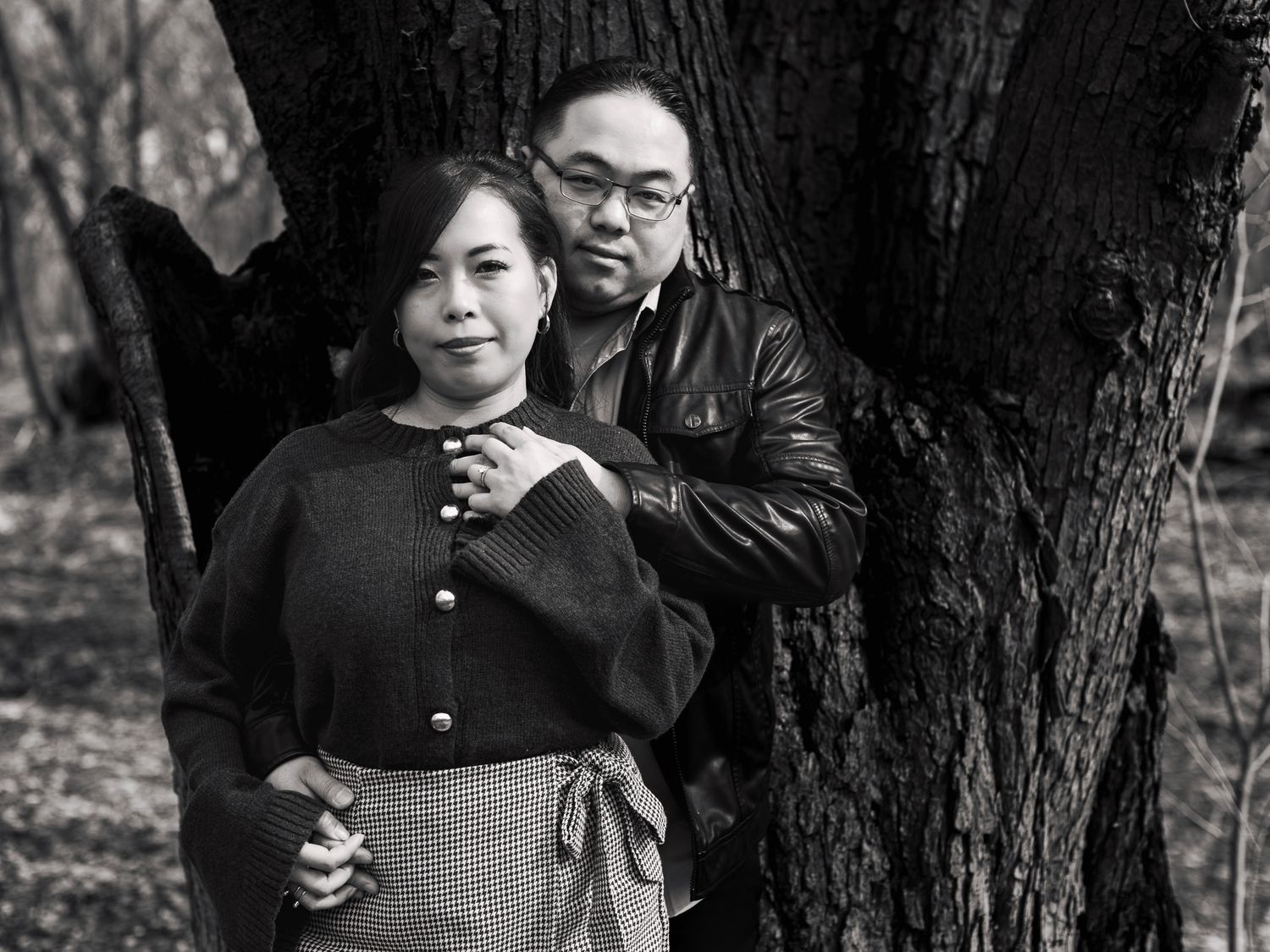 A vintage black and white photograph shows a couple posing together in a park setting near a tree.