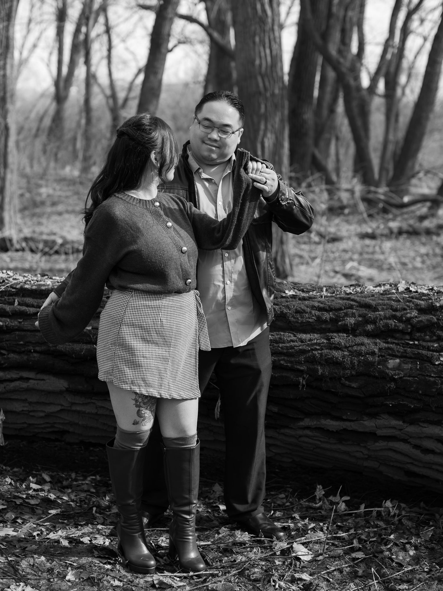 A couple in casual attire walks together through an autumn forest with fallen leaves on the ground.