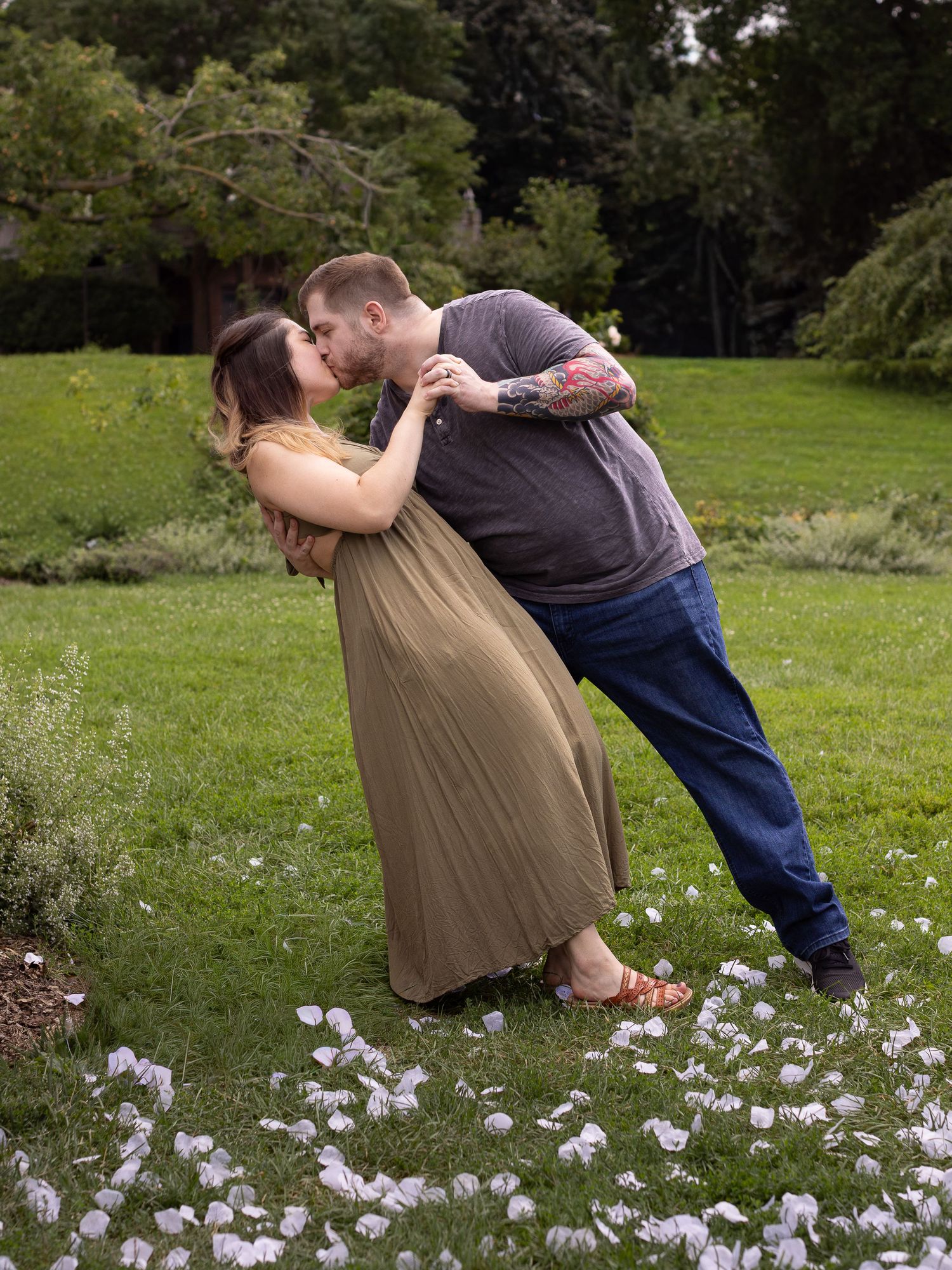 A romantic couple dips and dances together on a grassy meadow with delicate pink flowers scattered around them.