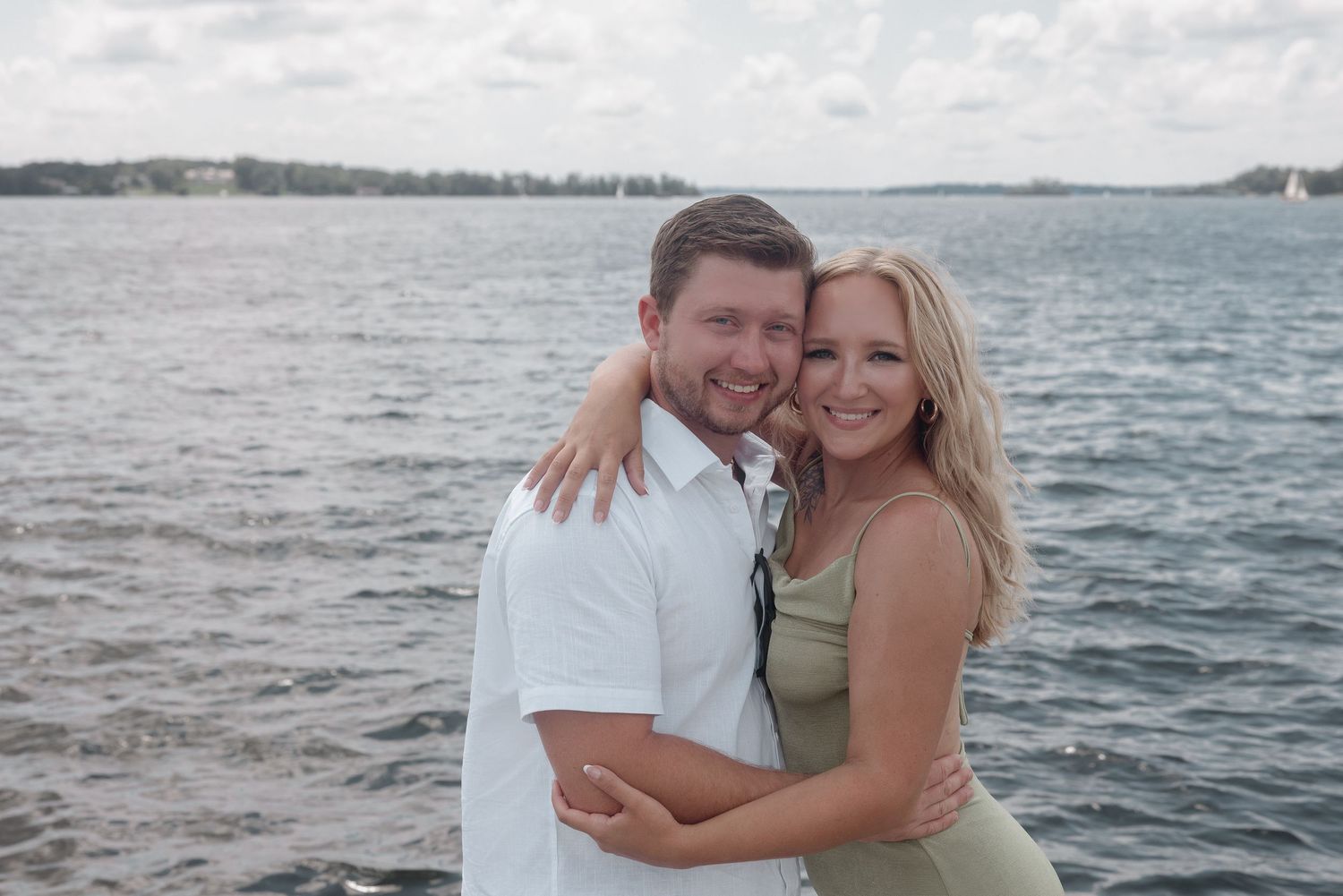 A couple embraces along the ocean waterfront during an engagement photography session on a cloudy day.