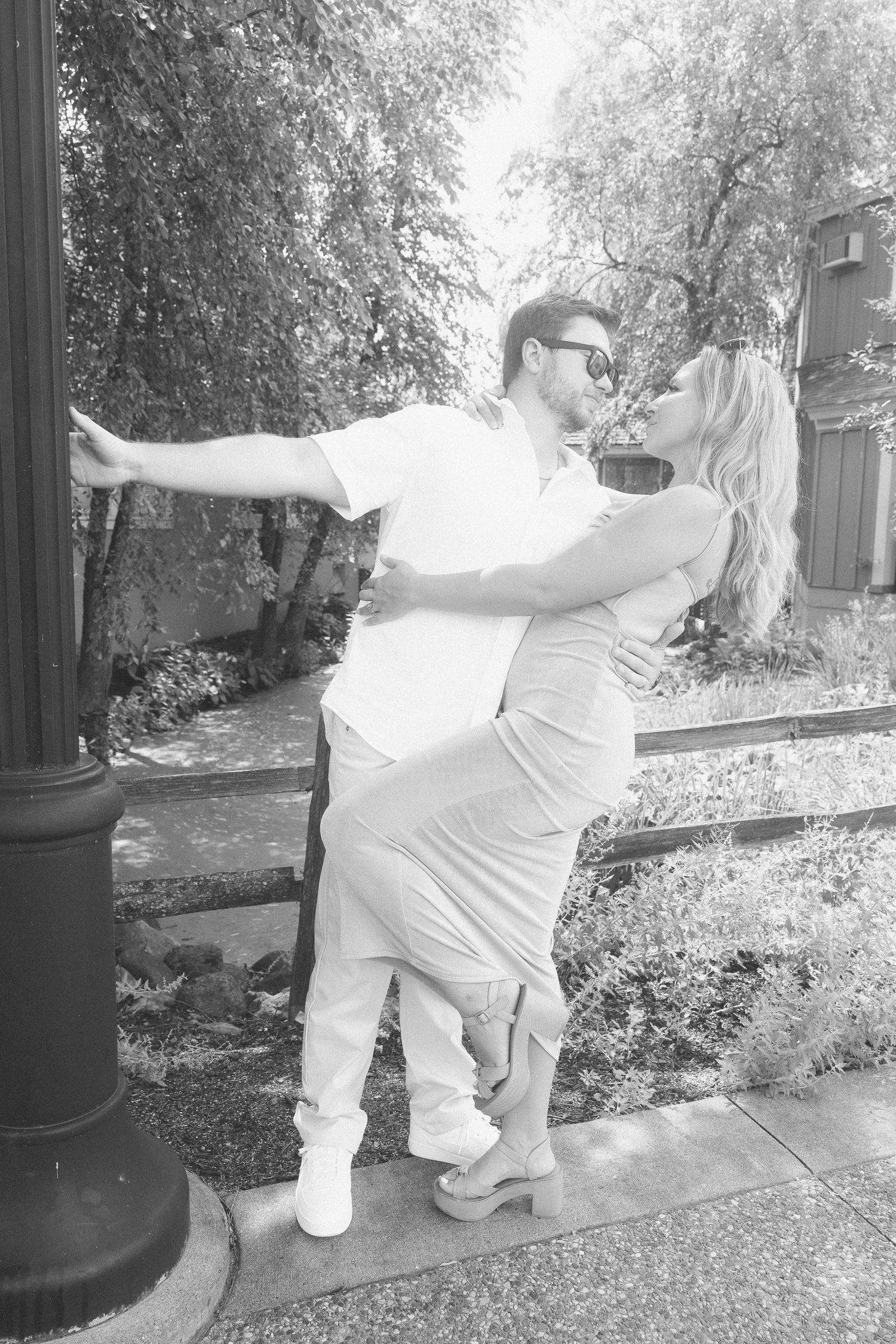 A sequence of black and white photos showing a couple dancing playfully on a sidewalk near trees.